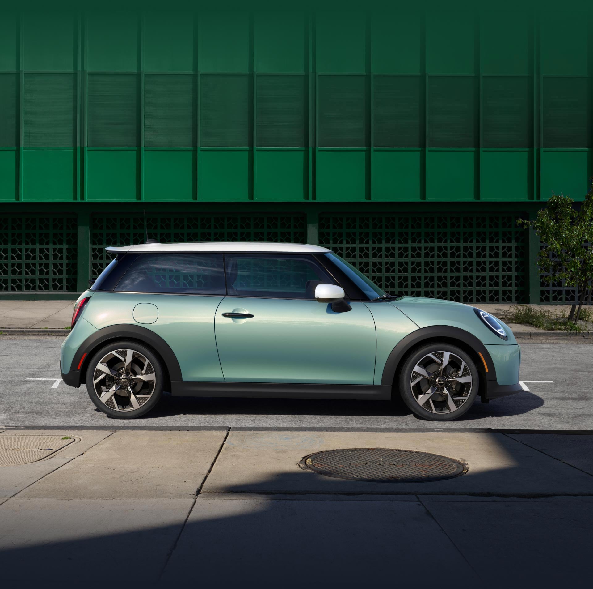 Side-view of a MINI Cooper S 2 Door in Ocean Wave Green Metallic parallel parked against a green wall.