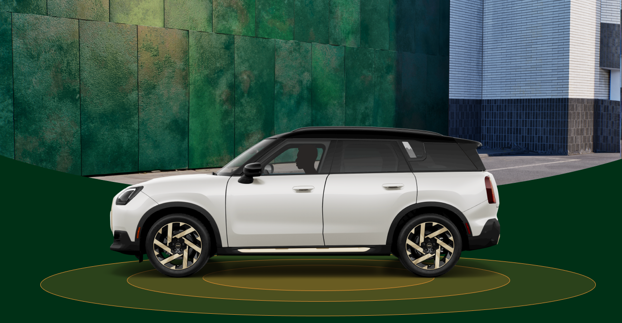 The side-view of a 2025 MINI Countryman SE ALL4 with orange rings beneath it against a blurred urban background.