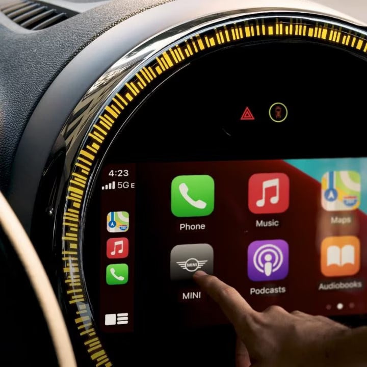 Closeup view of the touchscreen media display in a MINI vehicle, with a person’s index finger pointing at the MINI application button on its screen.