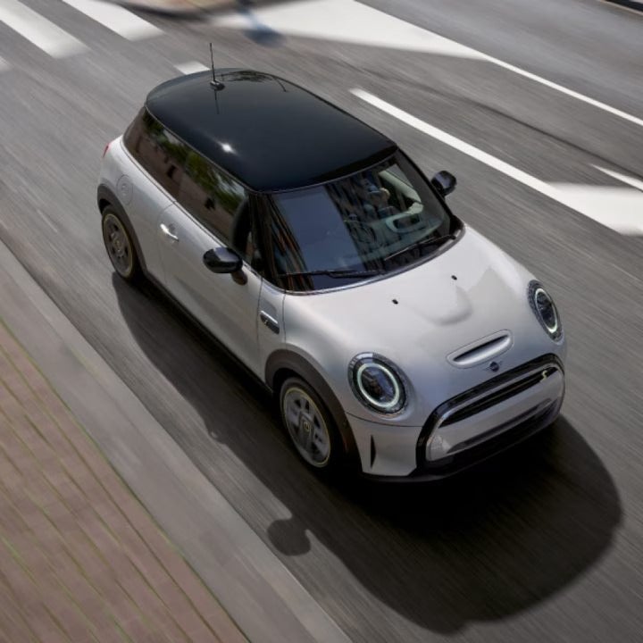 Overhead view of a white MINI Electric vehicle driving alone on a street with its shadow underneath it and its surroundings blurred out.